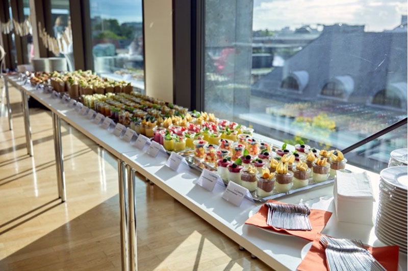 Buffet mit verschiedenen Desserts und Vorspeisen in Gläsern auf einem langen Tisch am Fenster.