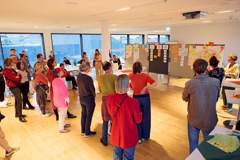 Teilnehmer einer Workshop-Runde betrachten und diskutieren Ergebnisse an Pinnwänden im Seminarraum.