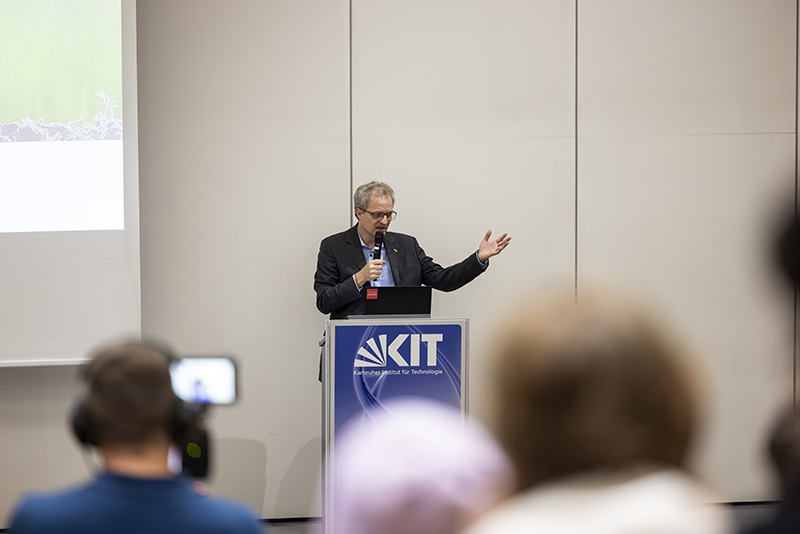 Mann hält Vortrag hinter Rednerpult mit KIT-Logo vor Publikum.