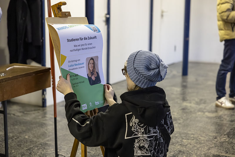 Eine Person hängt ein Poster der Veranstaltung auf.