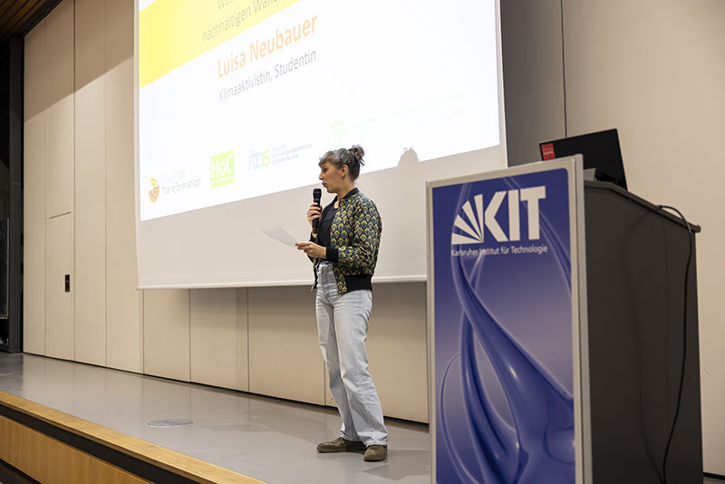 Person steht auf Bühne neben einem KIT-Podium und spricht.
