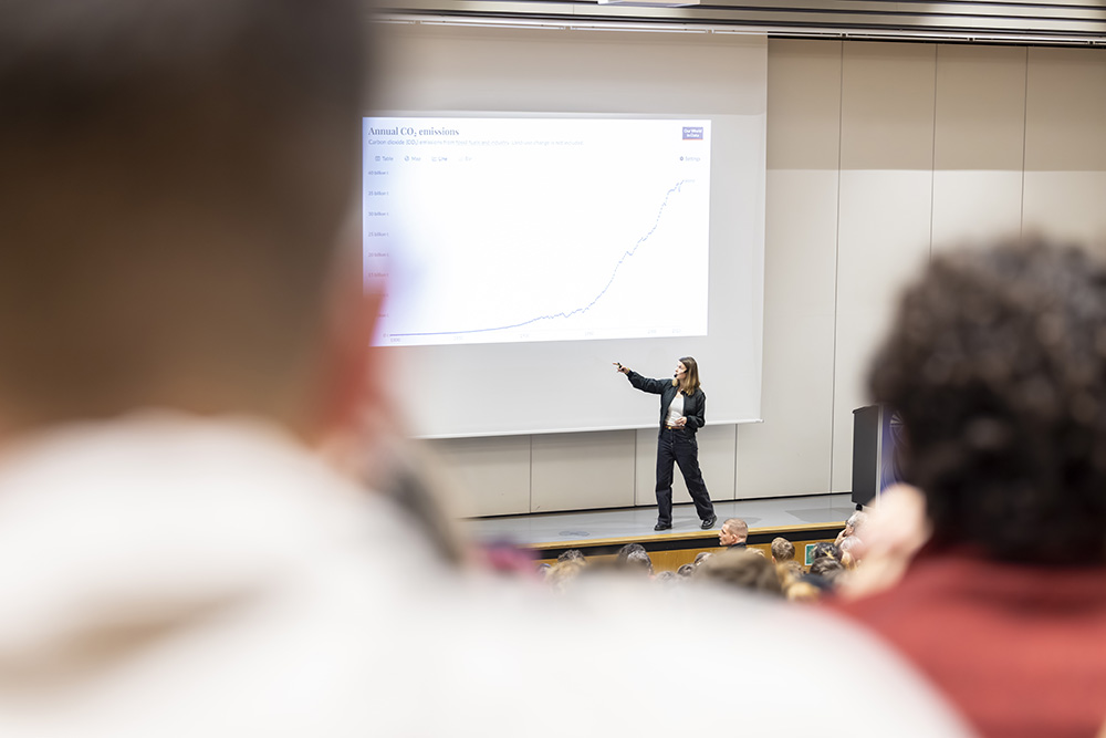 Frau präsentiert ein Diagramm an der Leinwand vor Publikum im Hörsaal.