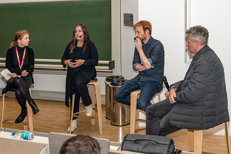 Vier Personen in eine Diskussion versammelt, sitzend auf Hockern im Seminarraum.