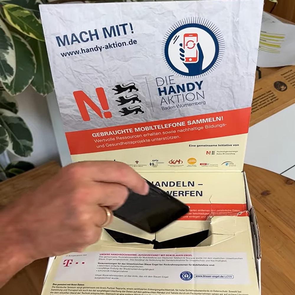 Smartphone wird von einer Person in eine Recyclingbox gegeben.