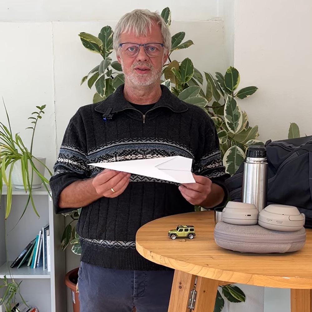 Volker Stelzer steht an einem Stehtisch und hält einen Papierflieger vor sich in der Hand.