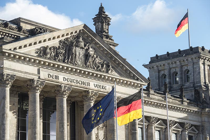 Detailansicht des Reichstagsgebäudes in Berlin mit der Aufschrift „Dem deutschen Volke“ und Flaggen.