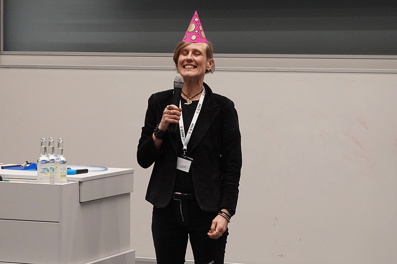 Lachende Frau mit Partyhut, die in ein Mikrofon spricht.