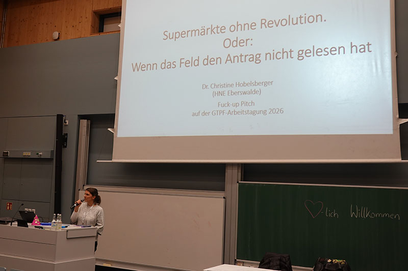 Frau hält einen Vortrag vor einer Präsentationsfolie auf einer Arbeitstagung.