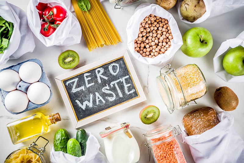 Lebensmittelreste und frische Zutaten rund um eine Schiefertafel mit „Zero Waste“.