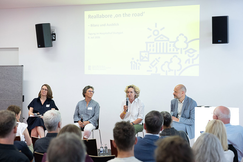 Gruppe von Menschen sitzt auf einer Bühne im Plenum und spricht zum Publikum über Reallabore.