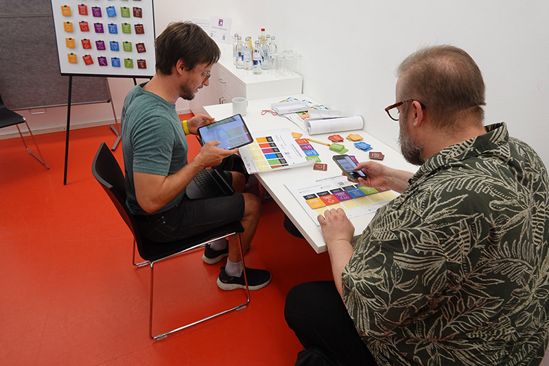 Zwei Personen sitzen an einem Tisch und gestalten ein Selbstexperiment mit bunten Karten.