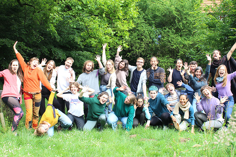 Gruppenfoto junger Menschen lachend und gestikulierend im Grünen.
