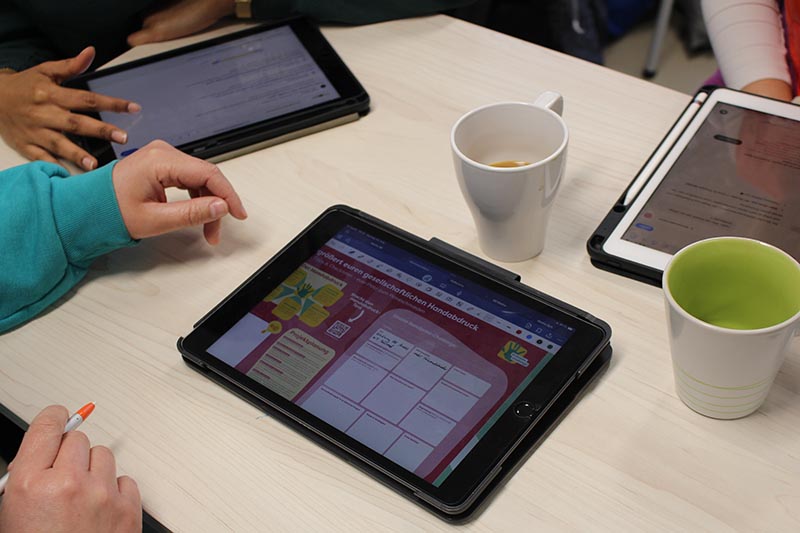 Personen arbeiten mit Tablets, auf dem Bildschirm ist ein Arbeitsblatt der climatechallenge zu sehen.