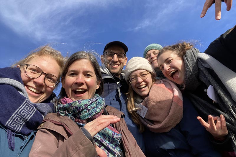 Gruppe lachender Menschen im Freien vor blauem Himmel.