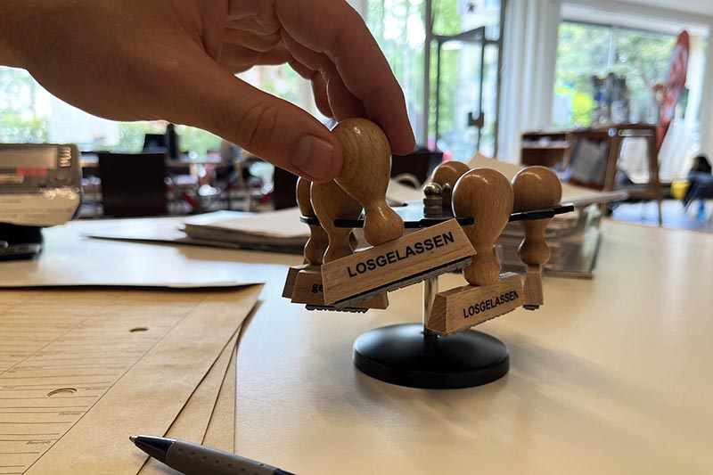 Hand greift nach einem Holzstempel mit der Aufschrift „LOSGELASSEN“.