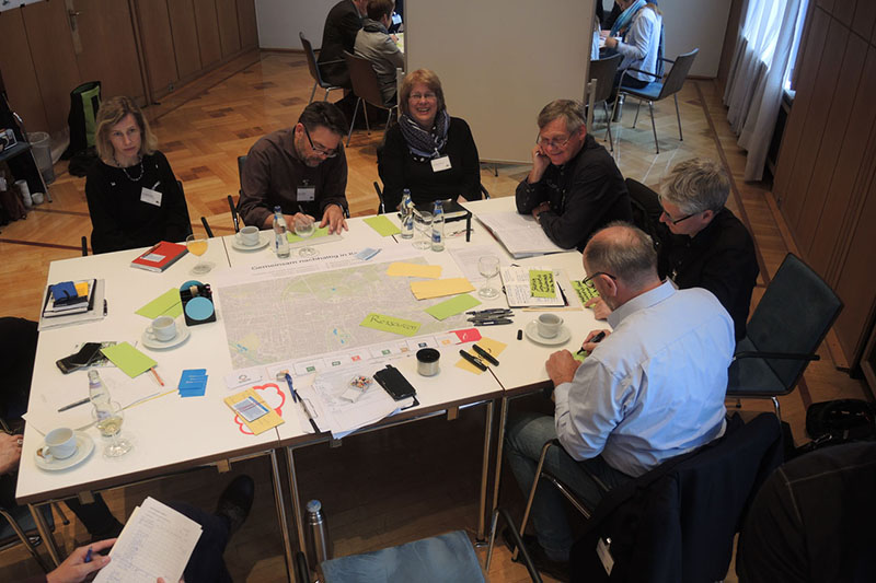 Gruppe von Erwachsenen sitzt an Tisch mit Karten und Spielbrett.