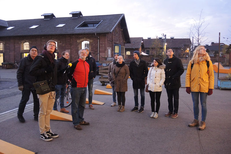 Menschen stehen im Freien vor einem Backsteinbau und blicken nach oben.