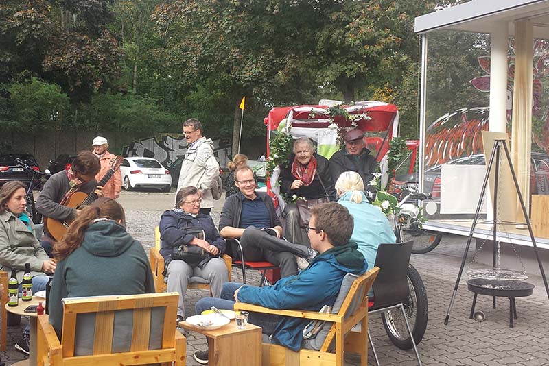 Gruppe von Menschen sitzt draußen vor dem Zukunftsraum und unterhält sich; gemütliche Atmosphäre.