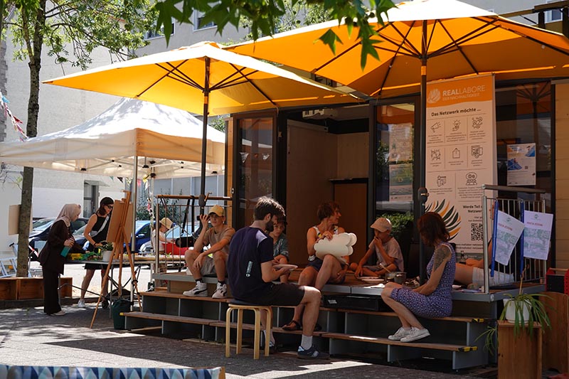 Personen sitzen im Freien vor dem MobiLab und unterhalten sich.